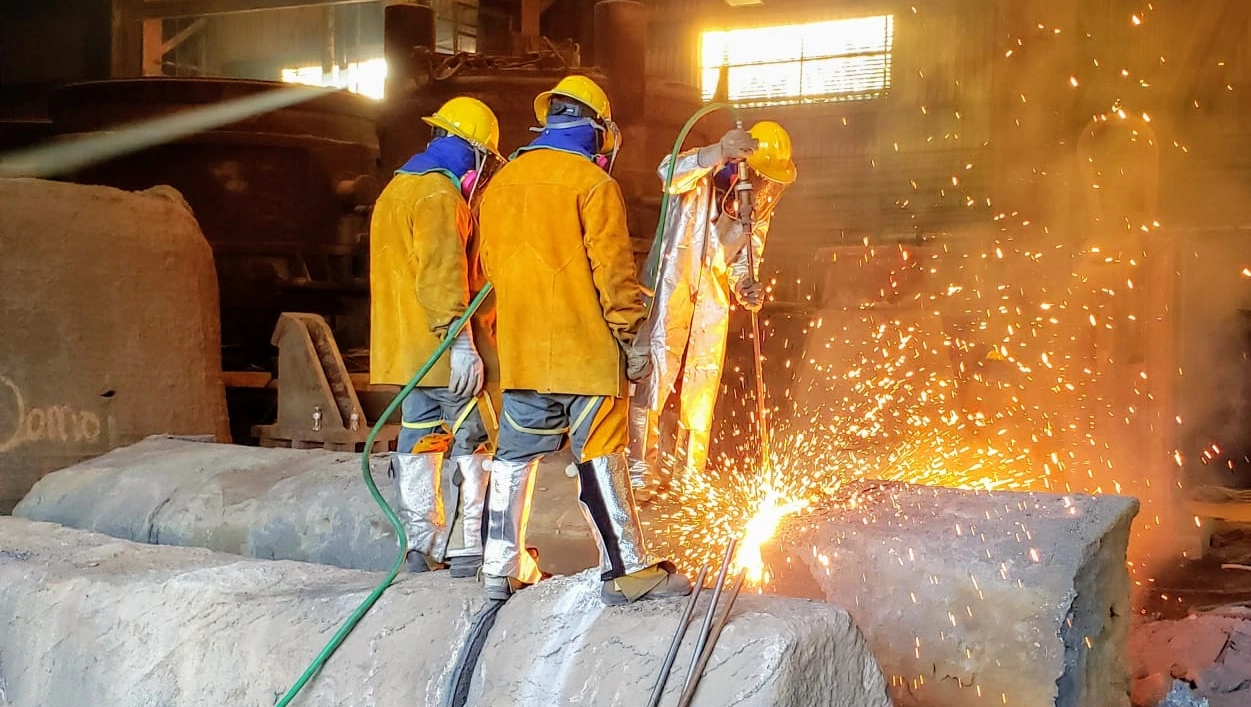 Scrap torching crew members cutting through metal with a torch in an industrial setting, with sparks flying